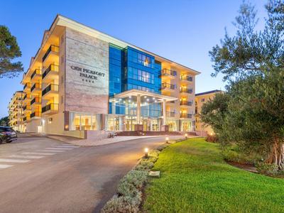 Moderno edificio alberghiero su più piani al tramonto con balconi illuminati e parcheggio.