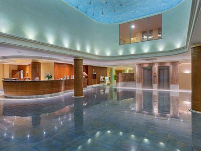 Ampia hall d'hotel con pavimento lucido, banco reception e illuminazione moderna sotto soffitto in vetro.