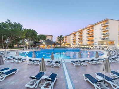 Grande piscina d'hotel con numerosi lettini e edifici sullo sfondo al crepuscolo.