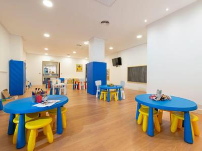 Stanza per bambini con tavoli e sedie colorati su pavimento in legno in ambiente luminoso.