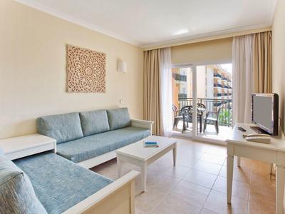 Soggiorno luminoso con divani blu, TV e balcone con vista su un edificio.