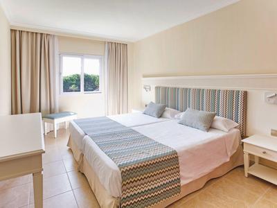 Camera d'albergo luminosa con letto matrimoniale, arredamento beige e finestra con tende.