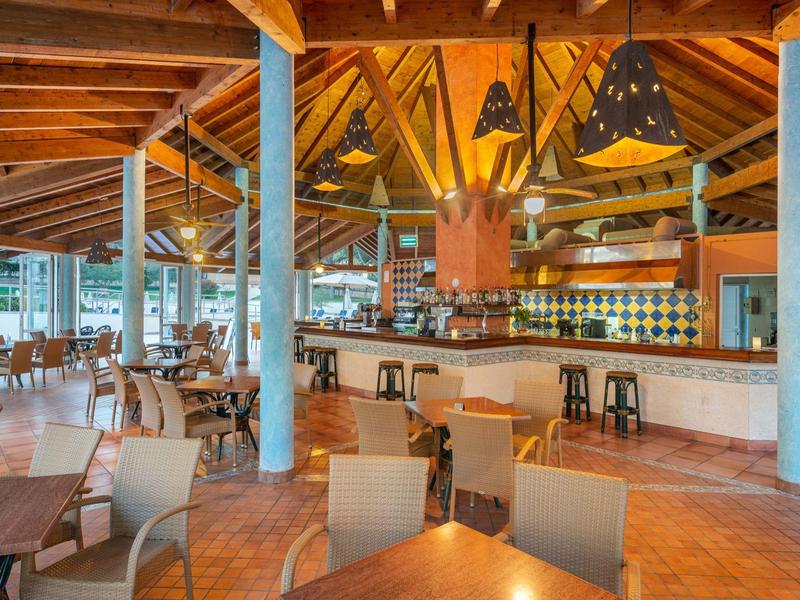 Ristorante all'aperto con mobili in legno, tetti e area bar in colori caldi.