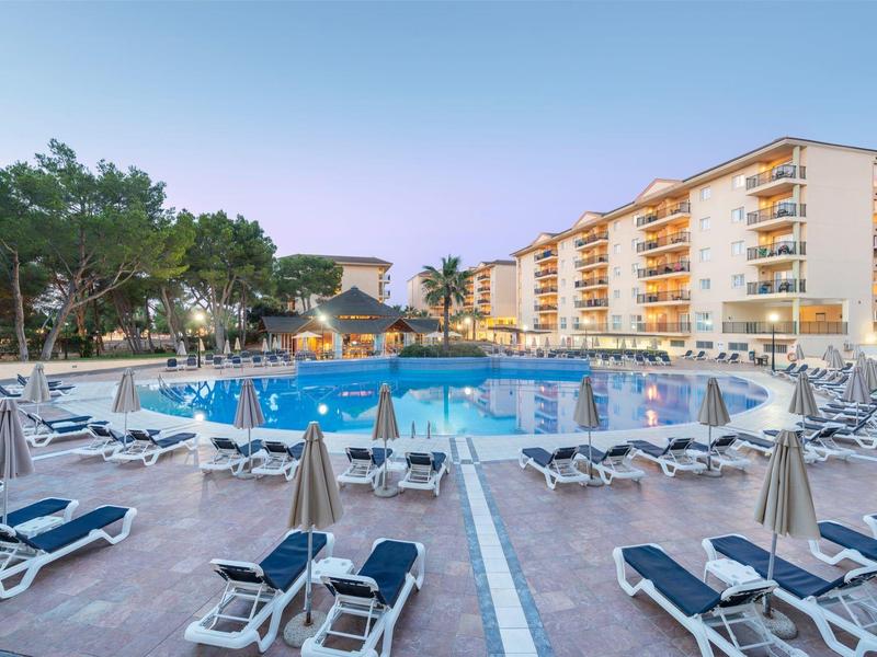 Grande piscina d'hotel con numerosi lettini e edifici sullo sfondo al crepuscolo.