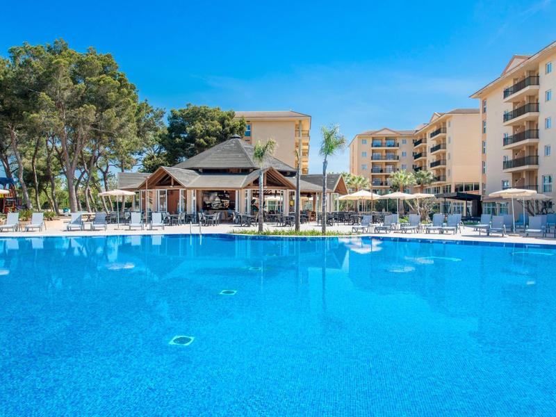 Grande piscina blu con lettini e edifici sullo sfondo sotto un cielo sereno.