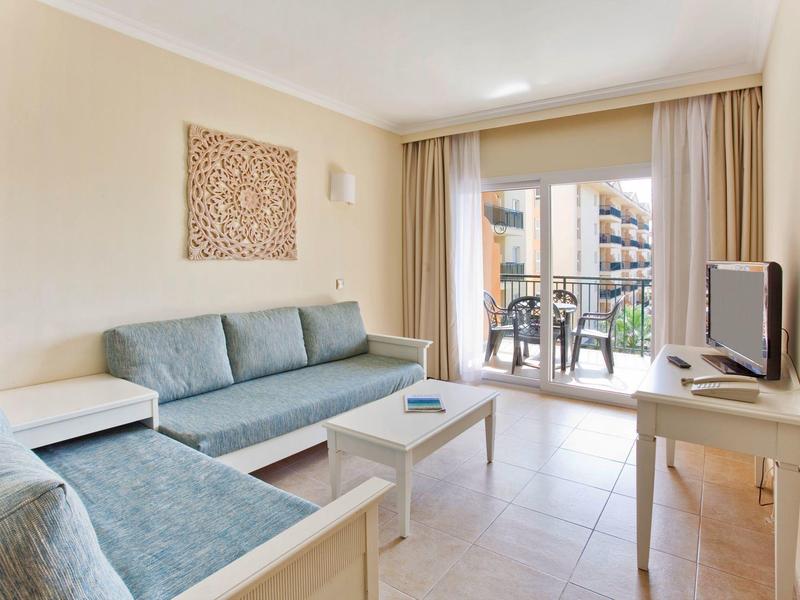 Soggiorno luminoso con divani blu, TV e balcone con vista su un edificio.