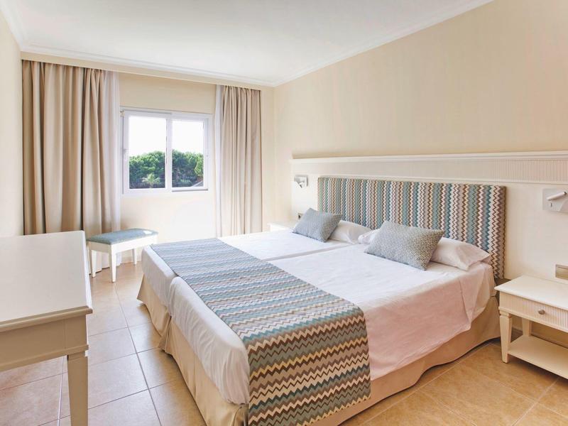 Camera d'albergo luminosa con letto matrimoniale, arredamento beige e finestra con tende.