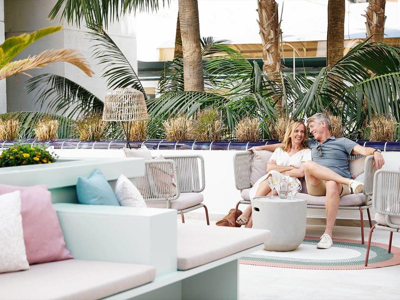 Pár odpočívá na lounge nábytku v tropické hotelové zahradě s palmami.