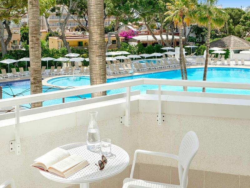 Balkon s stolem a židlí s výhledem na bazén a palmy v resortu.