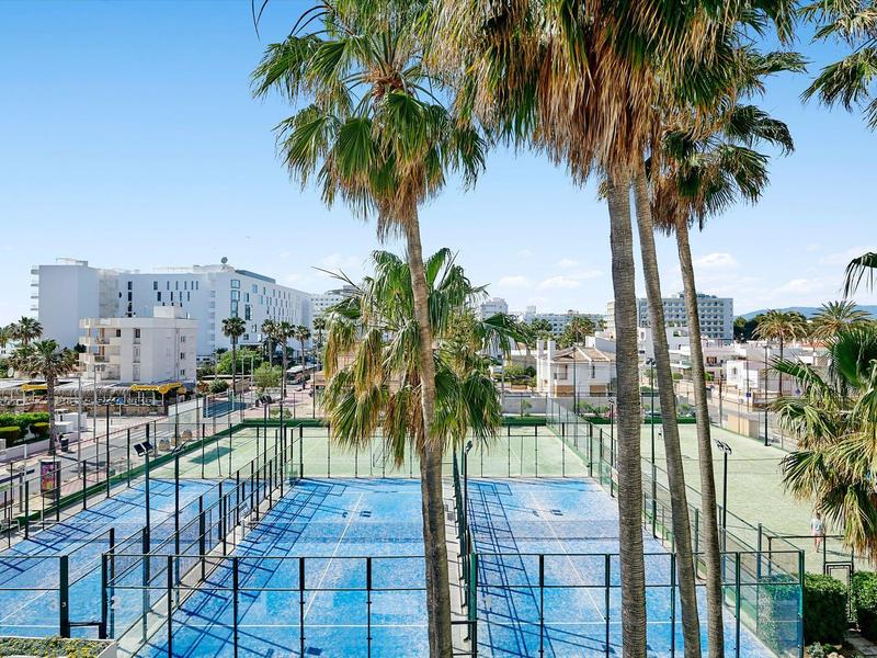 Moderní tenisové kurty s palmami před hotelem pod jasnou oblohou