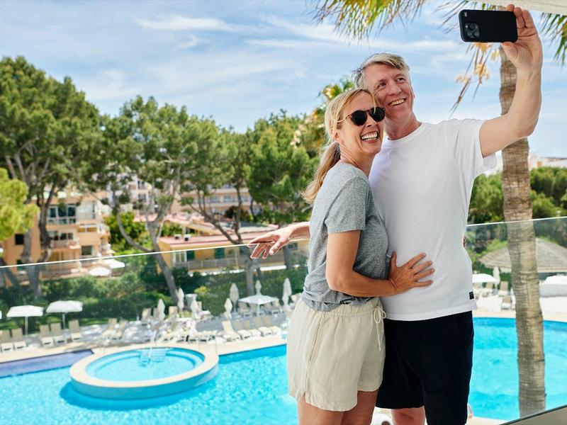 Pár si dělá selfie u bazénu v resortu za slunečného dne.