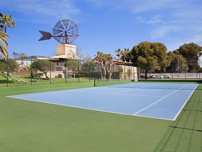 Ein Tennisplatz im Freien mit grünem und blauem Belag, umgeben von Palmen und einem Windrad im Hintergrund.