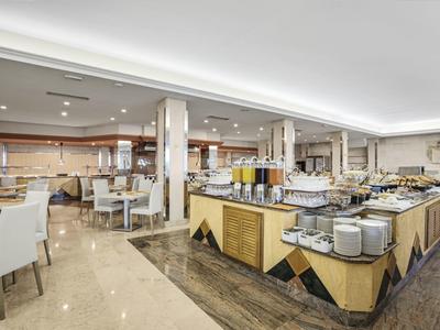 Velký bufet v prostorné hotelové restauraci s moderními stoly a židlemi.