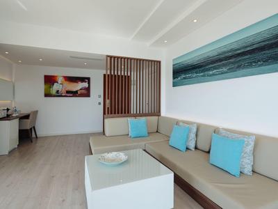 Moderní obývací pokoj s béžovou pohovkou, modrými polštáři, bílým stolkem a barevnými obrazy na stěně.