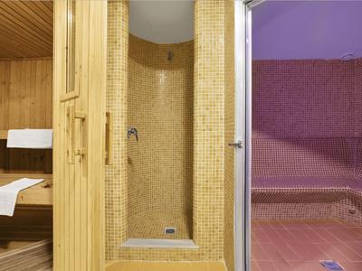 Dřevěná sauna s dlaždicovou sprchou a růžovou relaxační zónou vedle ní.