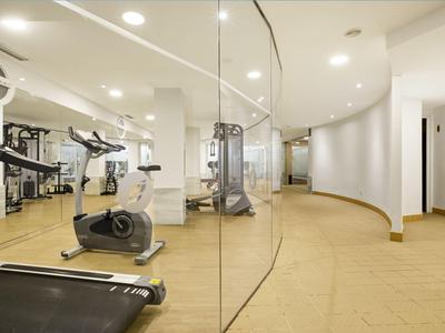 Moderner Fitnessraum mit Laufband, Fahrradergometer und anderen Fitnessgeräten in hellem Raum.