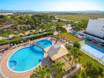 Hotelpool mit Liegebereich und Grünflächen in sonniger Landschaft nahe einem Hotelgebäude.