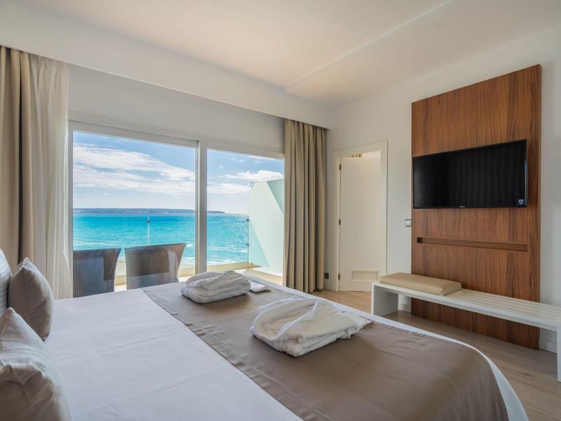 Elegantní hotelový pokoj s balkonem a výhledem na moře, televizí na stěně.