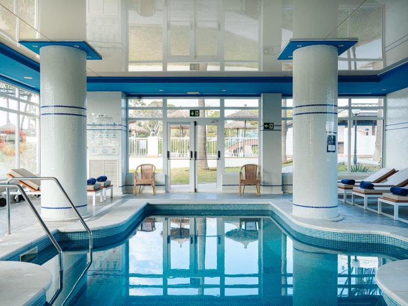 Moderní krytý bazén s bílými sloupy a modrými lehátky.