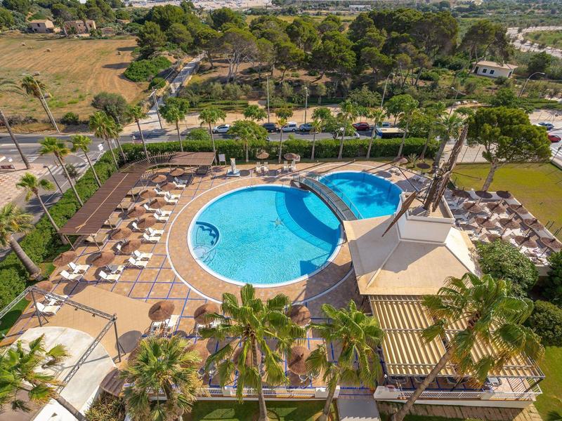 Kruhový bazén s osvětlenou terasou a lehátky obklopený zelení.