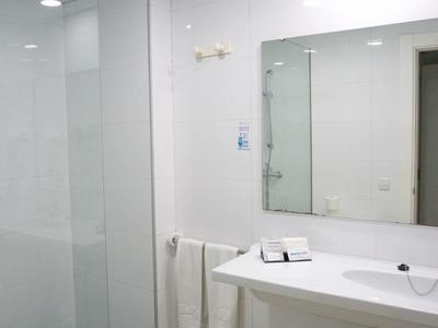 Espace de salle de bain blanc moderne avec lavabo, miroir, serviettes et cabine de douche.