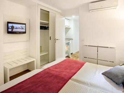 Chambre d'hôtel moderne avec lit double, couvre-lit rouge, armoire ouverte et TV murale.