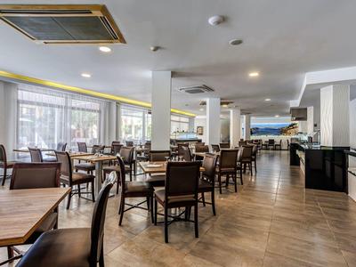 Restaurant lumineux avec sols en bois, tables en bois et chaises marron, grandes fenêtres.