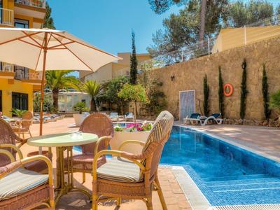 Terrasse ensoleillée avec tables, chaises et piscine à côté d'un bâtiment d'hôtel jaune.