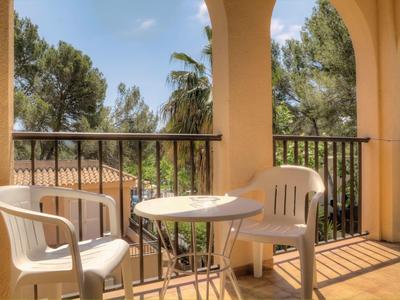 Balcon avec deux chaises en plastique blanc et une petite table avec vue sur des arbres et un ciel bleu