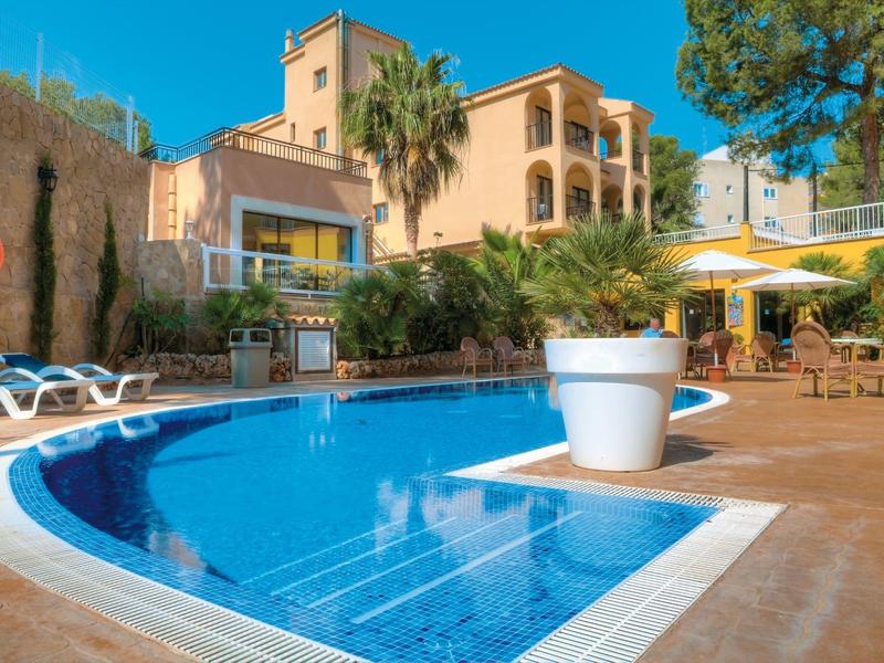 Hôtel avec piscine extérieure, chaises longues et palmiers sous un ciel clair