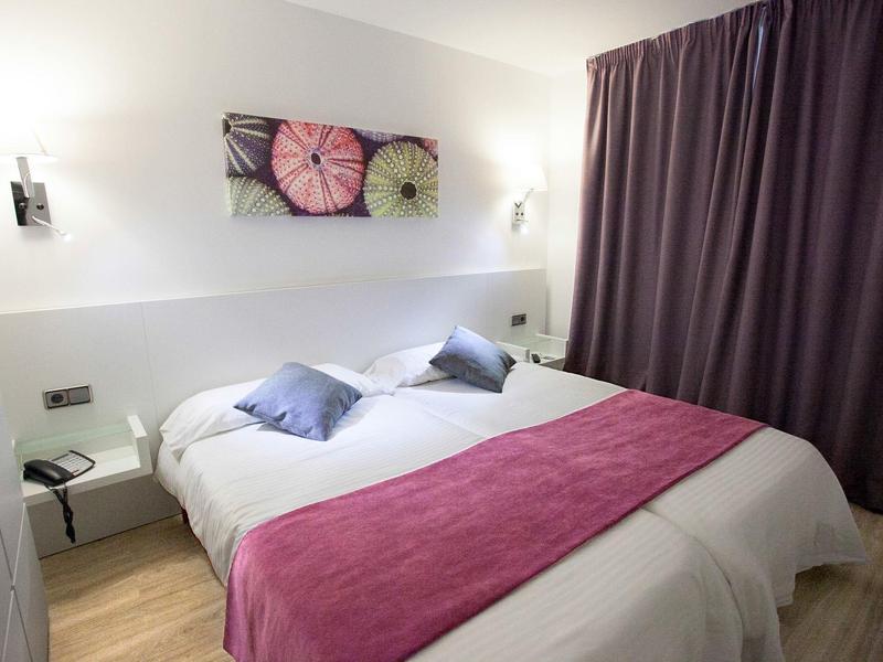 Chambre d'hôtel confortable avec lit double, rideaux violets et décoration murale.