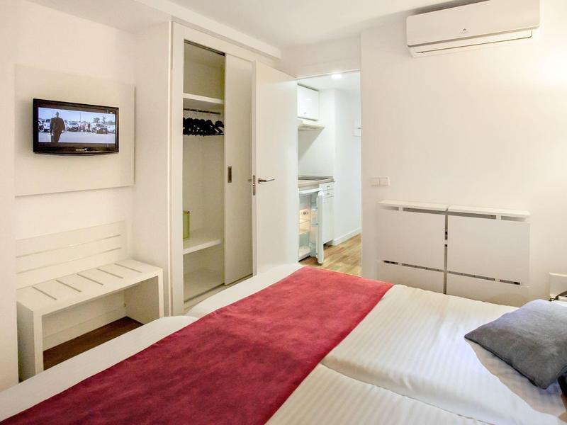 Chambre d'hôtel moderne avec lit double, couvre-lit rouge, armoire ouverte et TV murale.