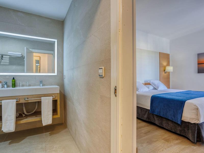 Vue d'une chambre d'hôtel avec salle de bain à gauche et chambre à coucher à droite, décorée de manière lumineuse