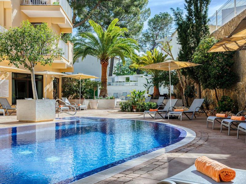 Piscine extérieure moderne avec chaises longues, parasols et arbres autour d'un hôtel.