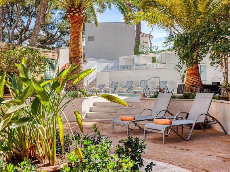 Terrasse ensoleillée avec des transats et des plantes tropicales à côté d'une piscine.