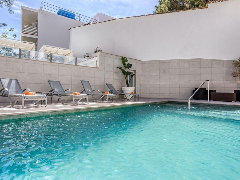 Espace piscine extérieur moderne avec chaises longues et plantes dans un hôtel.