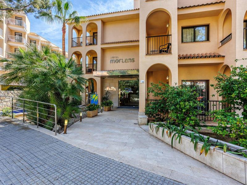 Entrée d'un hôtel à plusieurs étages avec une architecture méditerranéenne et une végétation luxuriante.