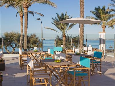 Outdoor seating area with tables and chairs under umbrellas beside palm trees near the ocean.
