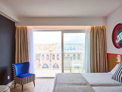 Bright hotel room with modern decor, blue and striped chairs, and a big window overlooking city buildings.
