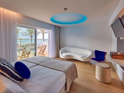 Modern hotel room with sea view, double bed, stylish seating, and a balcony overlooking the ocean.