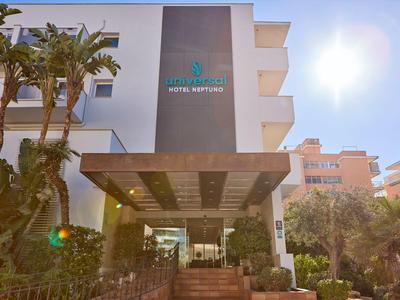 Entrance of a modern hotel on a sunny day with palm trees and blue sky.