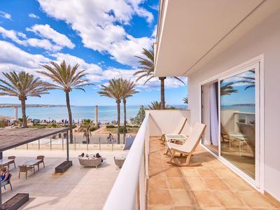 Balcony view of a beach resort with palm trees, lounge chairs, and outdoor seating under blue sky.