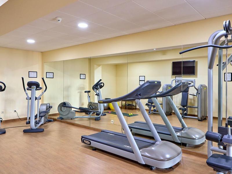 Hotel gym with treadmills, exercise bikes, and weight machines on wooden flooring.