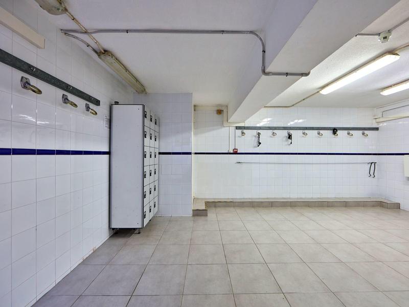 Empty hotel locker room with white tiled walls and floor, blue stripe and ceiling lights.