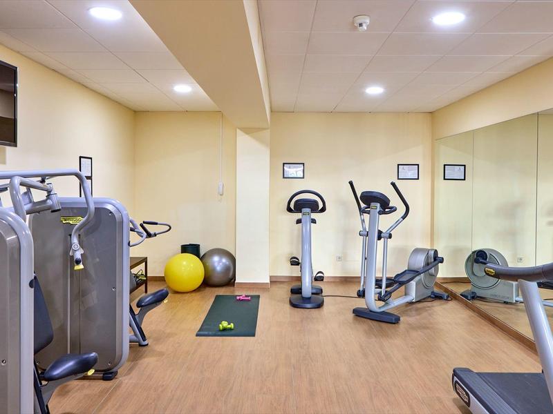 Bright gym with cardio machines, weights, exercise balls, and a large mirror.