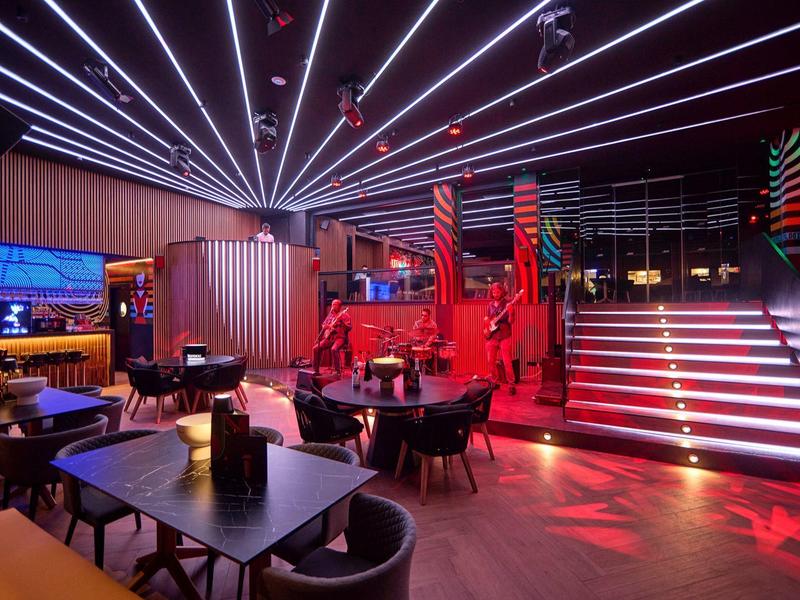Modern hotel lounge with dark decor, red lighting, seating area, and illuminated staircase.