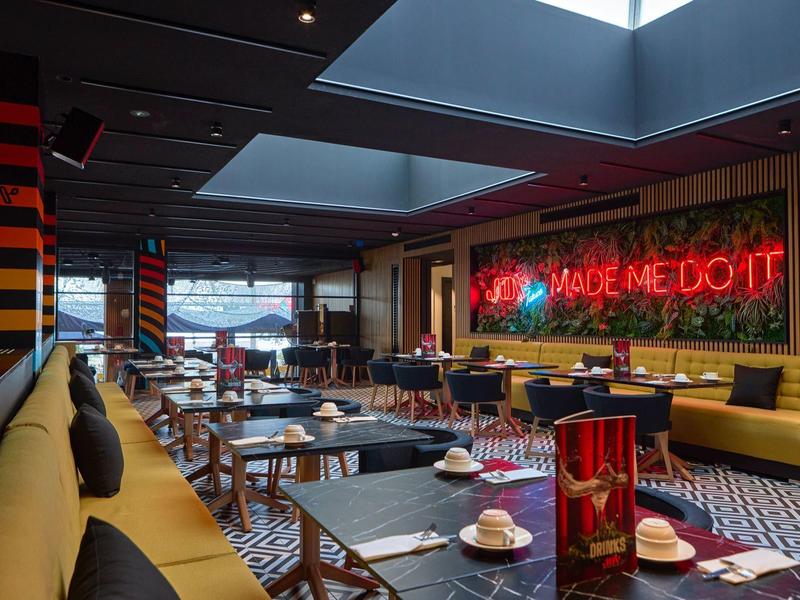 Modern hotel lounge with yellow sofas, neon sign, and black tables set for coffee.
