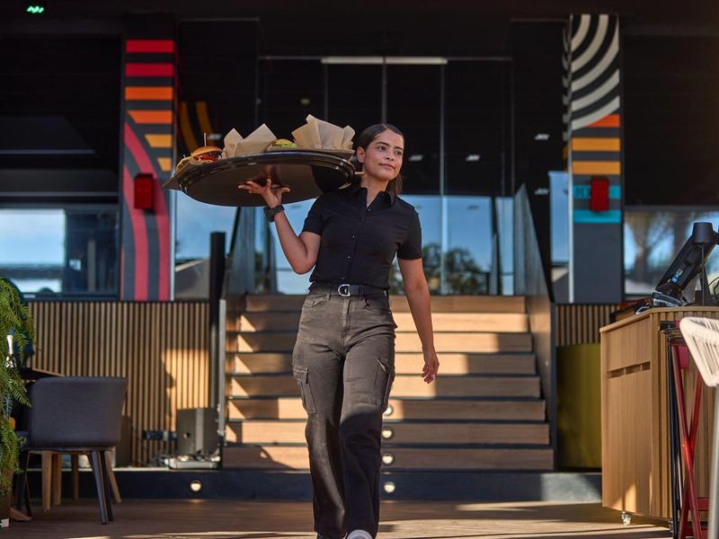 Waitress carrying a tray of food in a modern restaurant with colorful wall patterns.
