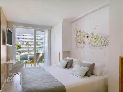 Modern eingerichtetes Hotelzimmer mit Doppelbett, Schreibtisch und Balkon mit Blick auf Außenanlage.