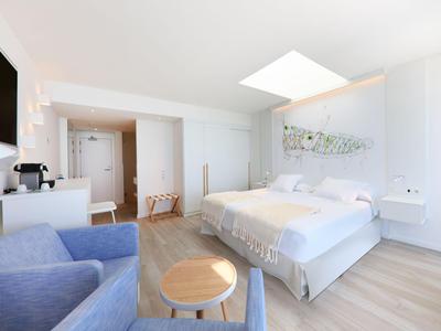 Modernes Hotelzimmer mit Doppelbett, zwei Sesseln und hellem Holzboden unter natürlichem Licht.